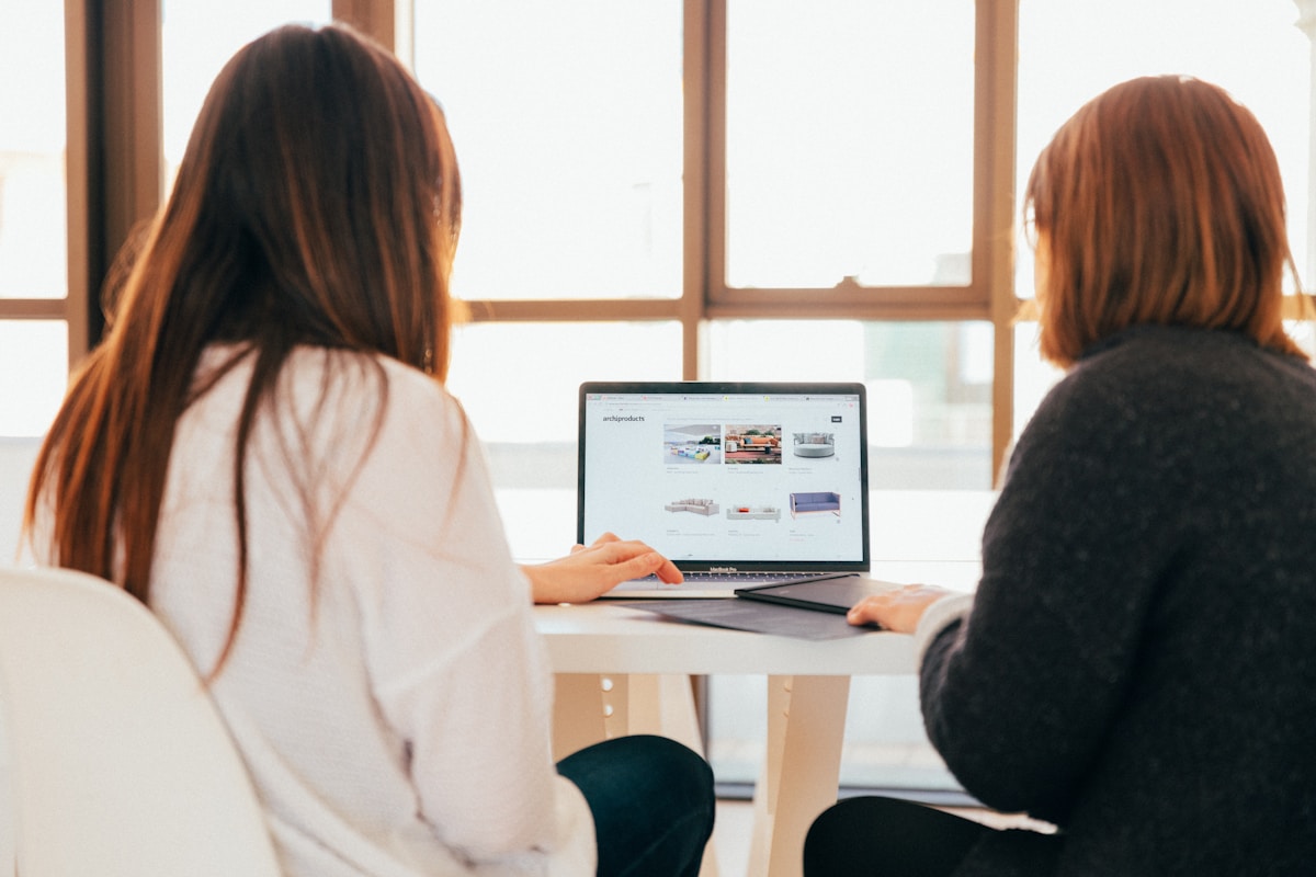 Como começar a criar um site para sua empresa? two women talking while looking at laptop computer