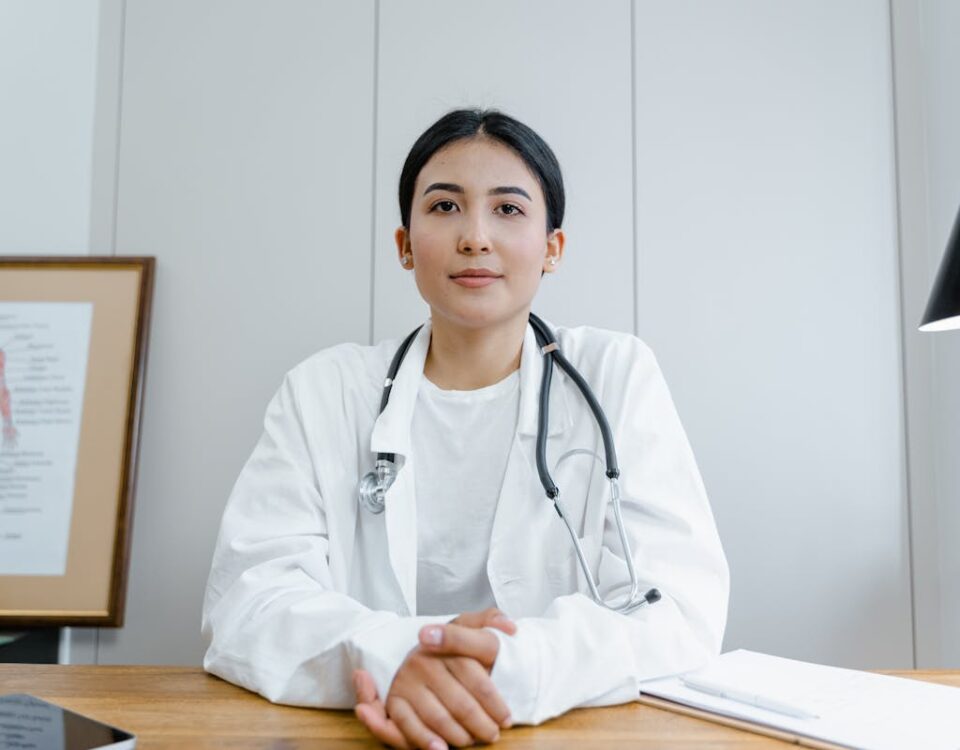 Como saber se seu médico é bem avaliado? Young female doctor sitting at desk with stethoscope, ready for telehealth consultation.