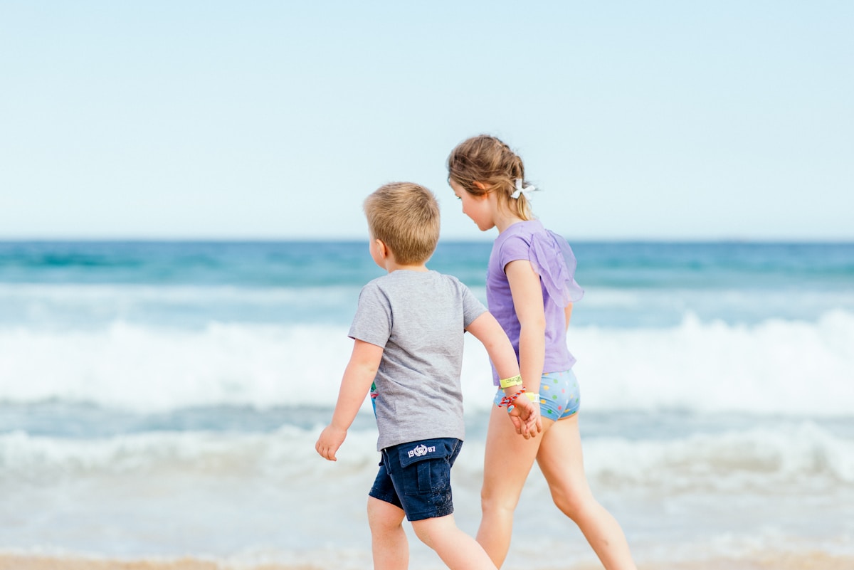 Como escolher o melhor tecido para roupas infantis? boy in white t-shirt and blue shorts standing on seashore during daytime