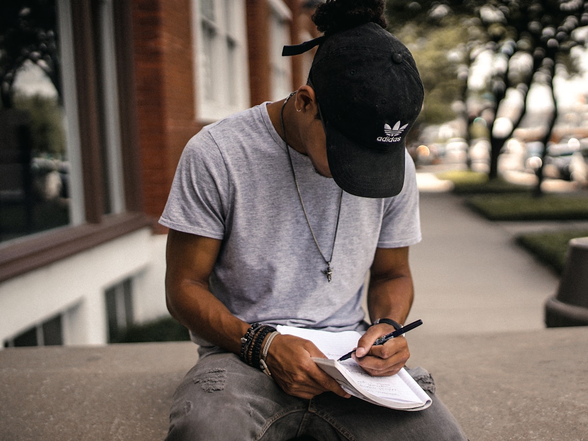 Qual método de estudo combina com sua rotina? person in black adidas cap sitting on bench writing on notebook