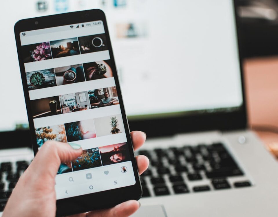 O que faz um painel SMM ser eficiente? A person uses a smartphone to browse social media in front of a laptop, emphasizing modern technology and lifestyle.