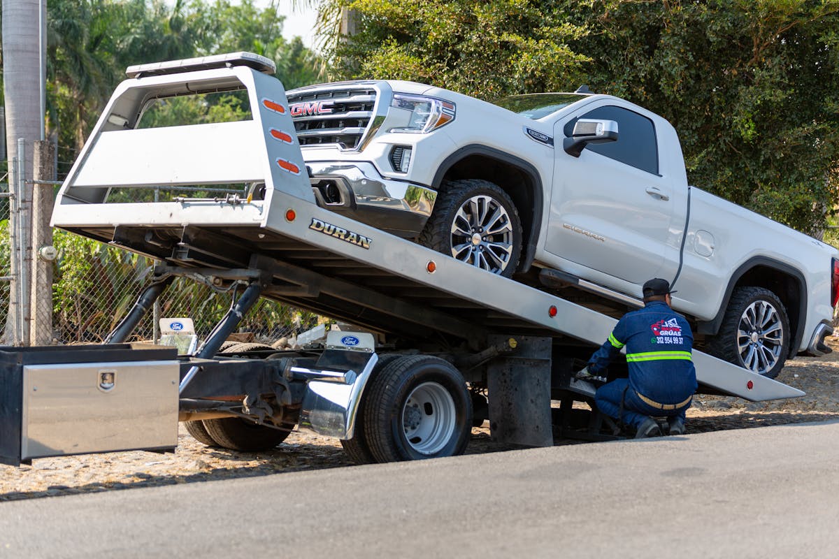 Como funcionam os serviços de guincho no Brasil? Tow truck operator loading white GMC pickup truck on street in daytime.