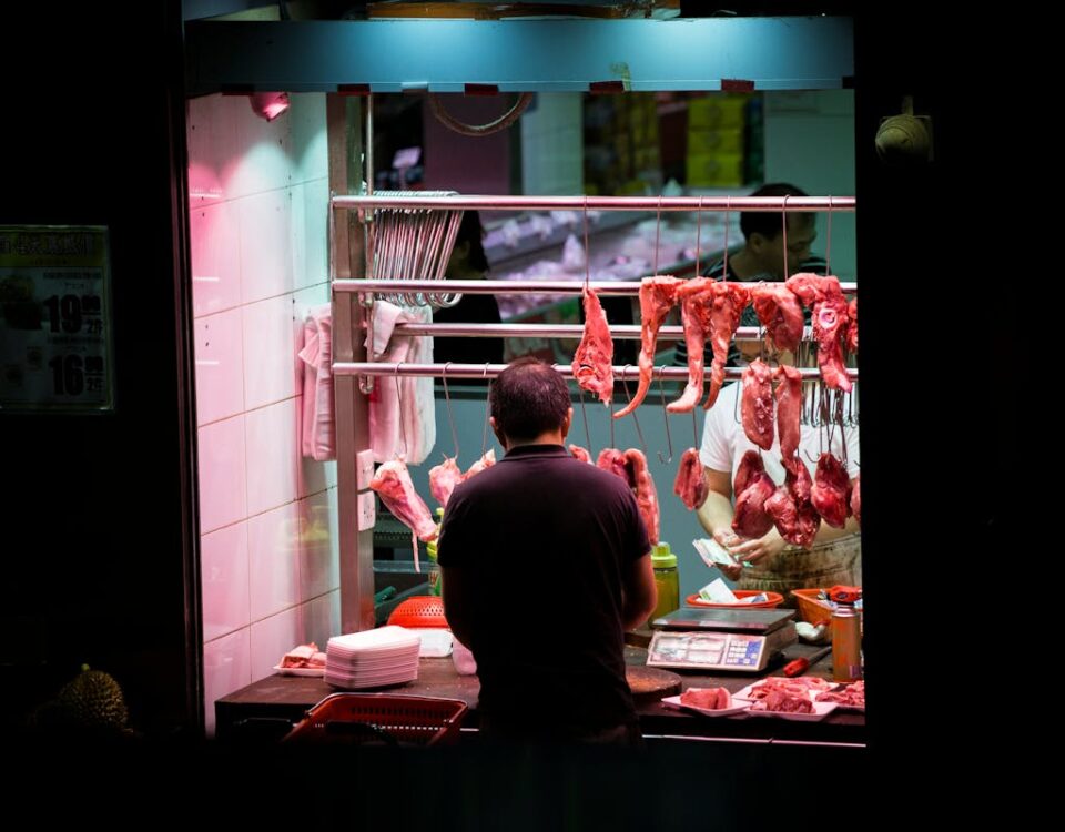 Qual a diferença entre resfriar e congelar cargas? Butcher working in a vibrant Hong Kong market stall preparing fresh cuts of meat.