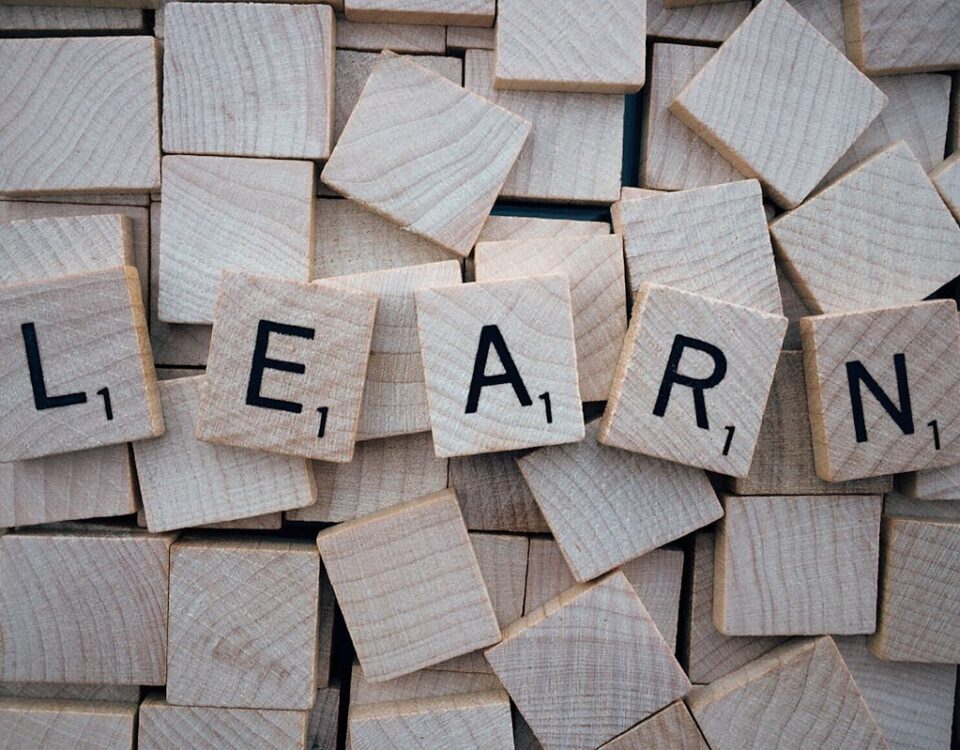 Qual o idioma mais fácil de aprender para brasileiros? Wooden letter tiles arranged to spell 'learn' on a background of scattered tiles.