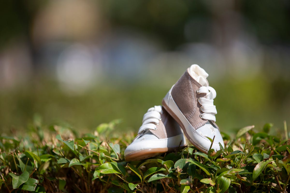 Pair of baby shoes resting on green leaves outdoors, emphasizing nature and style.