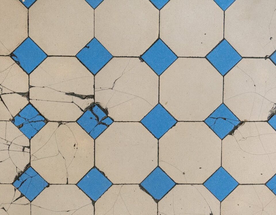 Como identificar problemas ocultos na sua casa Top view of a cracked geometric tile pattern featuring blue diamond tiles on a beige background.