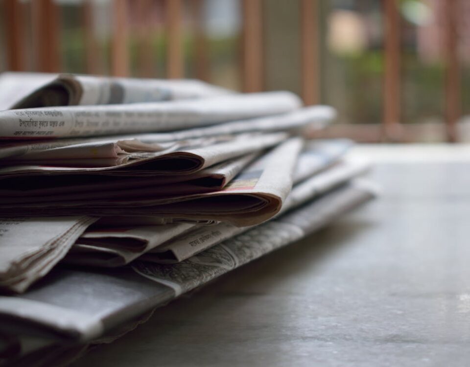 Notícias boas existem? Por que elas quase nunca aparecem? A close-up of a stack of newspapers resting on a desk, symbolizing information and media.