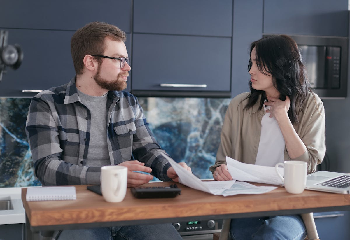 A young couple sitting at a table discussing bills and financial plans in a modern kitchen.