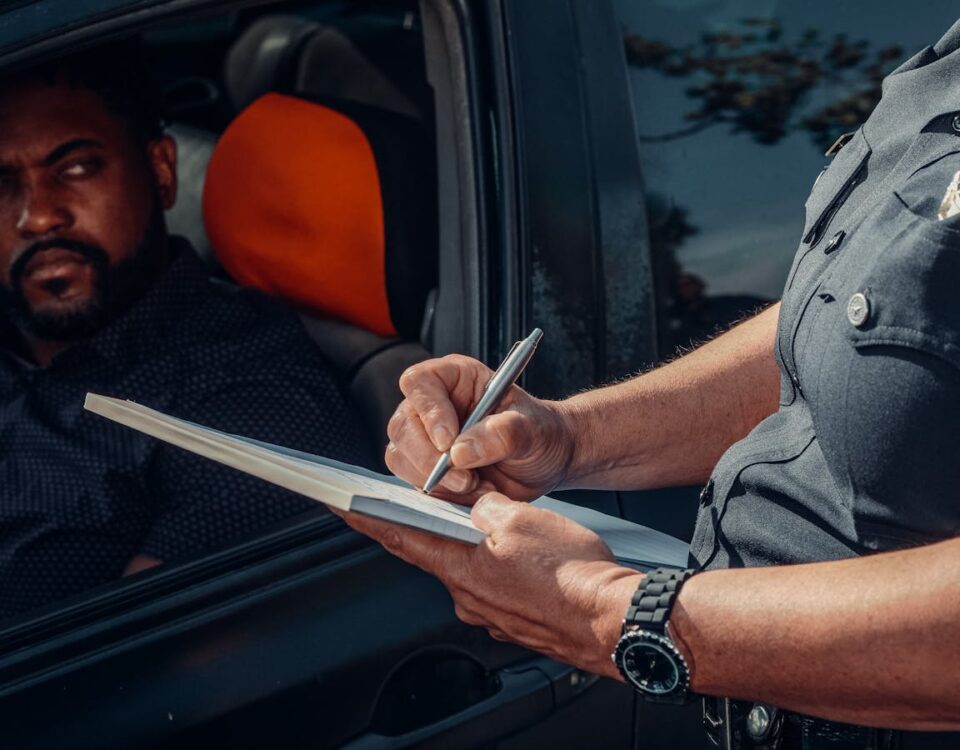 O que acontece se minha CNH expirar? A police officer writes a ticket as the driver looks on from inside the car.