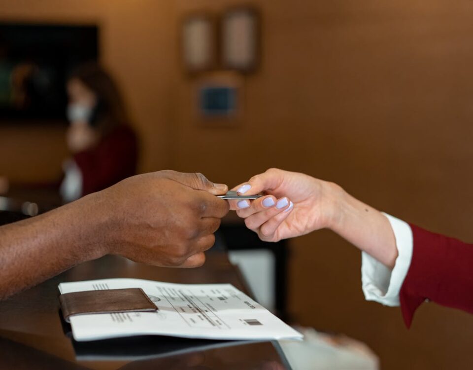 Por que contratar um despachante vale a pena? Close-up of a hotel receptionist receiving a credit card from a guest, highlighting a transaction at check-in.