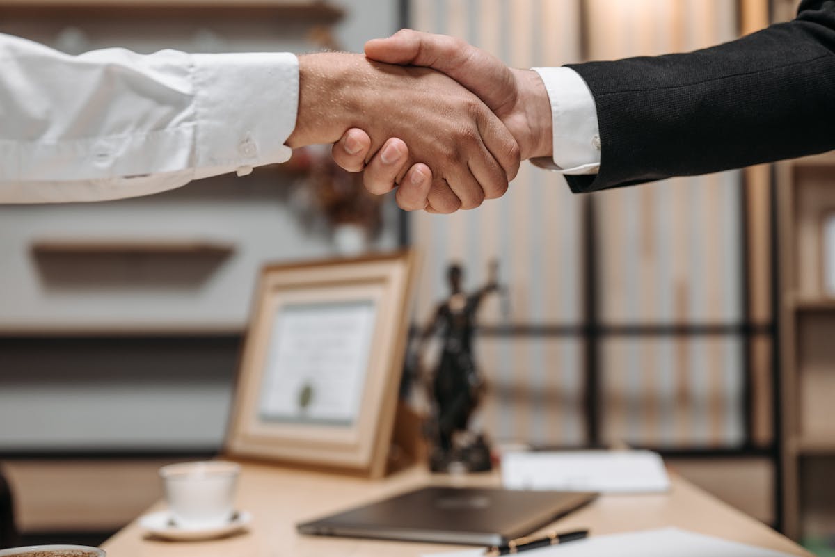 Como saber se um advogado criminalista é confiável? Close-up of a handshake between two professionals in a modern office setting, emphasizing partnership and agreement.