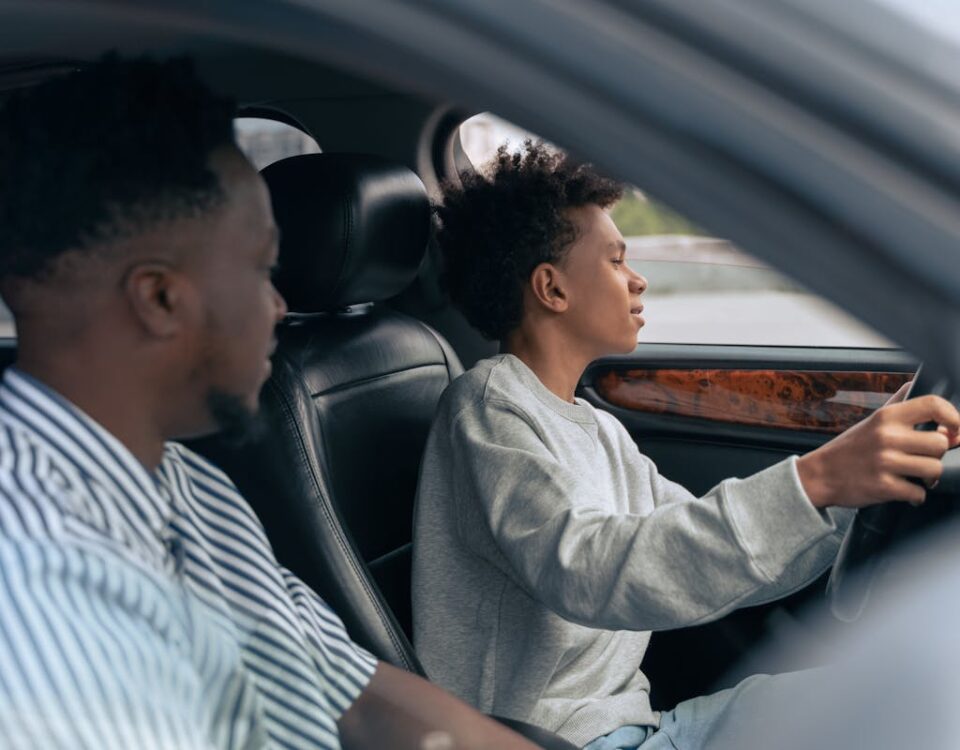 Quais mitos cercam o processo de tirar a CNH? A father teaches his son to drive, sitting together in a car and discussing techniques. Side view indoors.