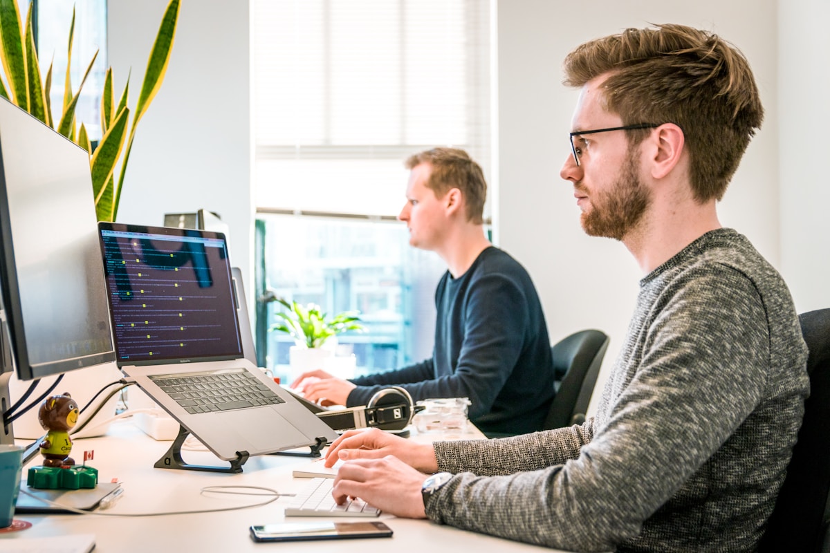 Como melhorar o conforto no trabalho sem gastar muito? man sitting on chair wearing gray crew-neck long-sleeved shirt using Apple Magic Keyboard