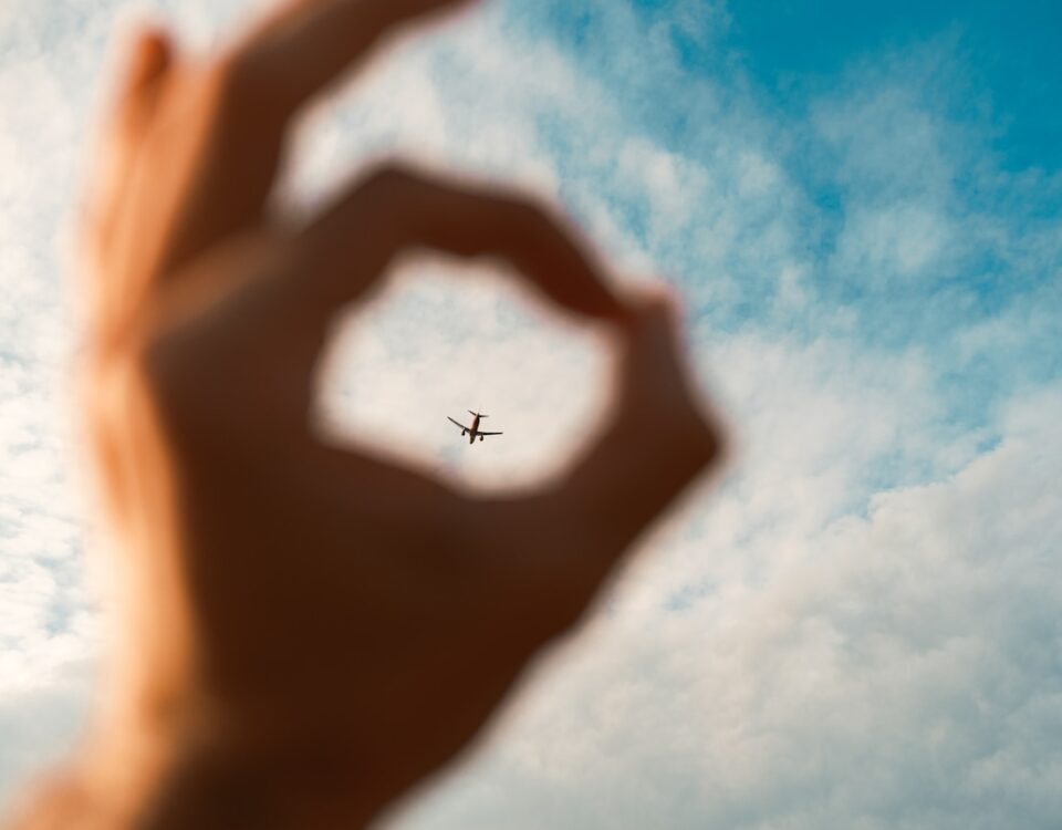 Por que guardamos lembranças de viagens? a hand making a heart shape with an airplane in the background