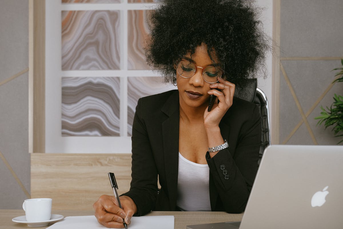 Como otimizar o atendimento sem aumentar os custos? Businesswoman making a phone call while working at the desk, focused and professional.
