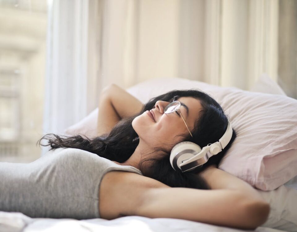 Por que certos sons parecem mais agradáveis? A woman with headphones lying on a bed, enjoying music in a relaxed, cozy setting.