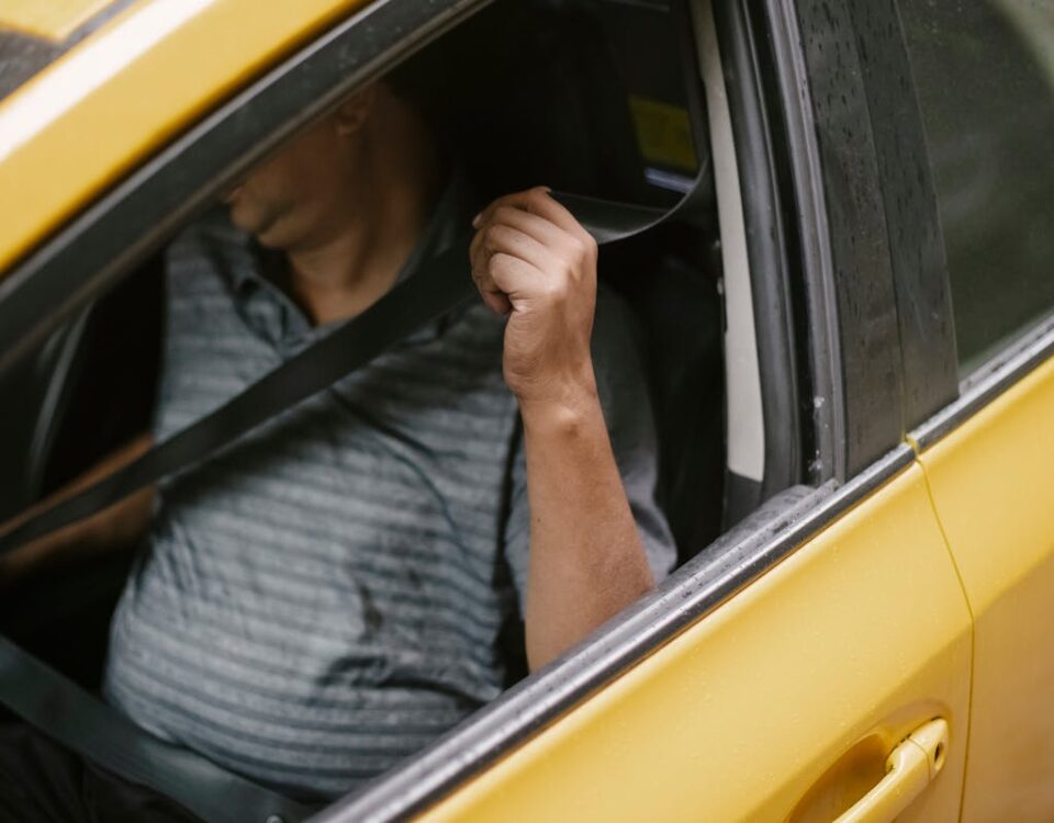 Direção defensiva realmente evita acidentes? A man securely fastens his seatbelt inside a yellow taxi, emphasizing safety during urban transport.