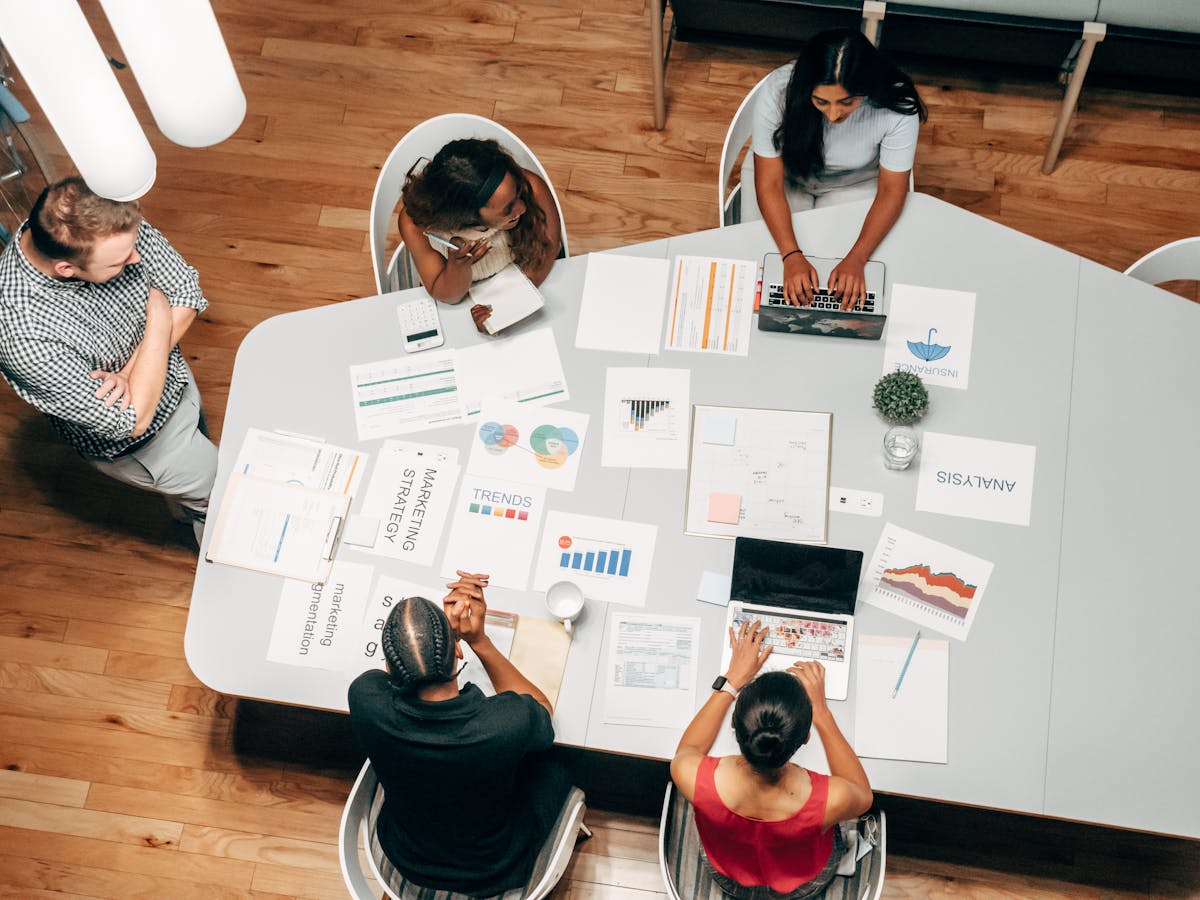 Qual o momento certo para contratar uma agência criativa? A diverse group working on marketing strategies with charts and laptops in an office setting.