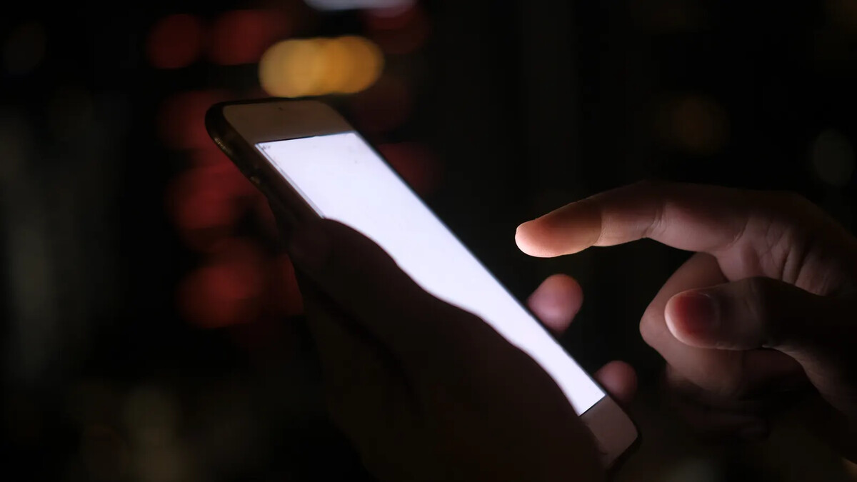 Mão segurando smartphone à noite com luzes da cidade desfocadas ao fundo