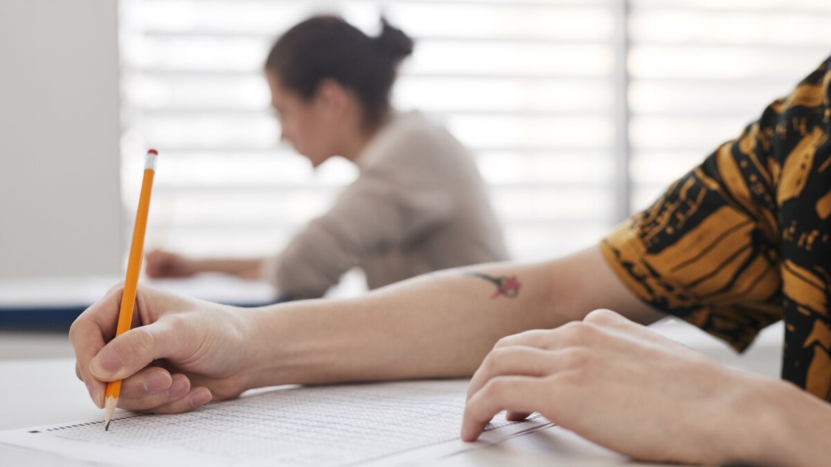 Mão de estudante segurando lápis sobre folha de prova