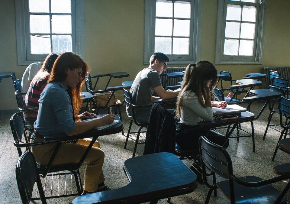 Estudantes fazendo prova em sala de aula com janelas altas