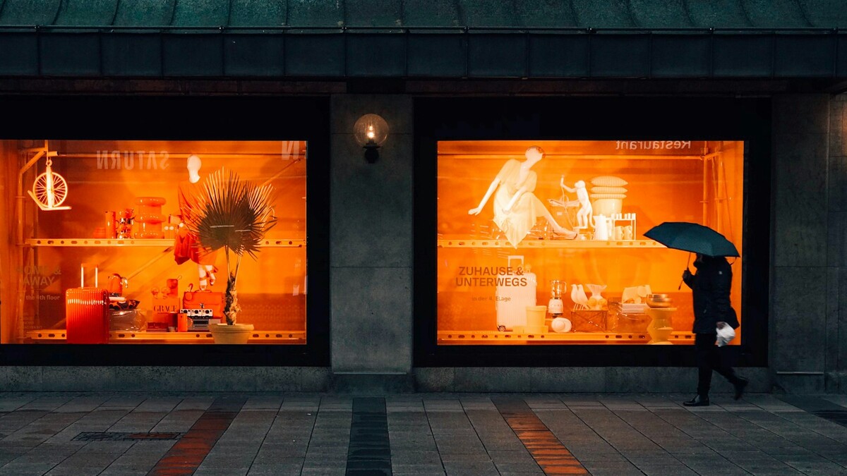 Pessoa com guarda-chuva passa por vitrine iluminada à noite