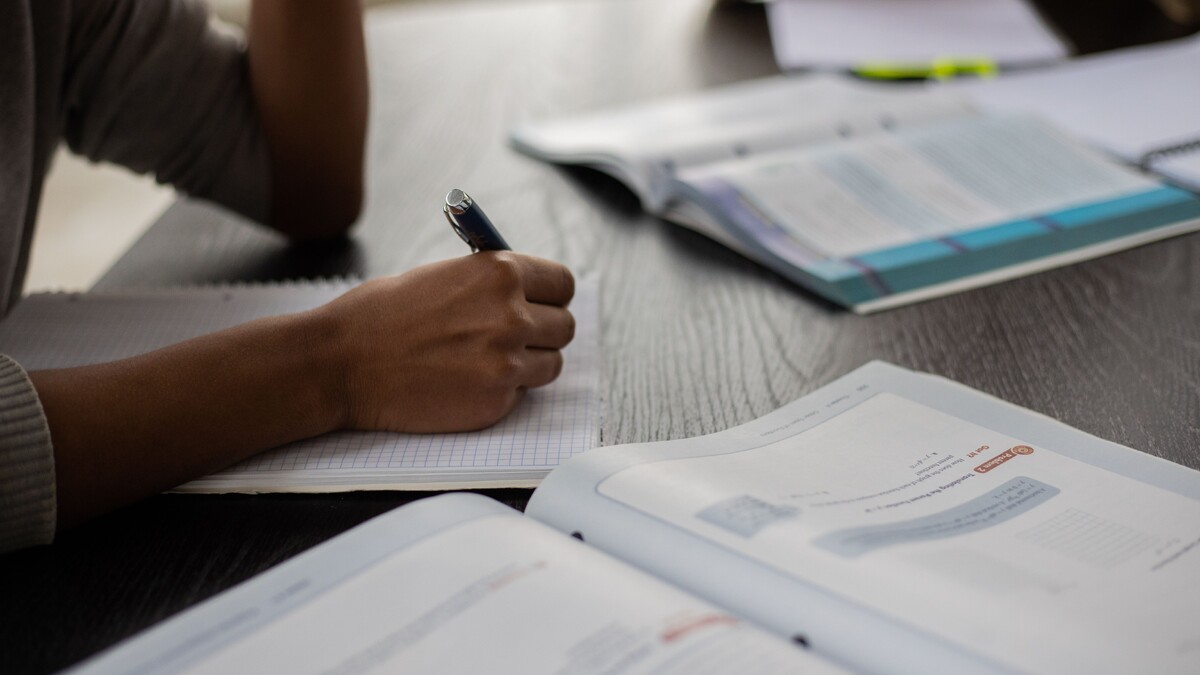 Local de prova do Enem 2026 liberado: como consultar o cartão Estudante faz anotações ao lado de livros em uma sala