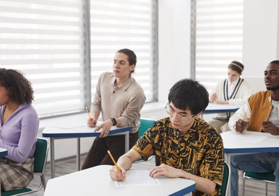 Local de prova do Enem 2026 liberado: como consultar o cartão Estudantes escrevendo durante uma prova em sala de aula