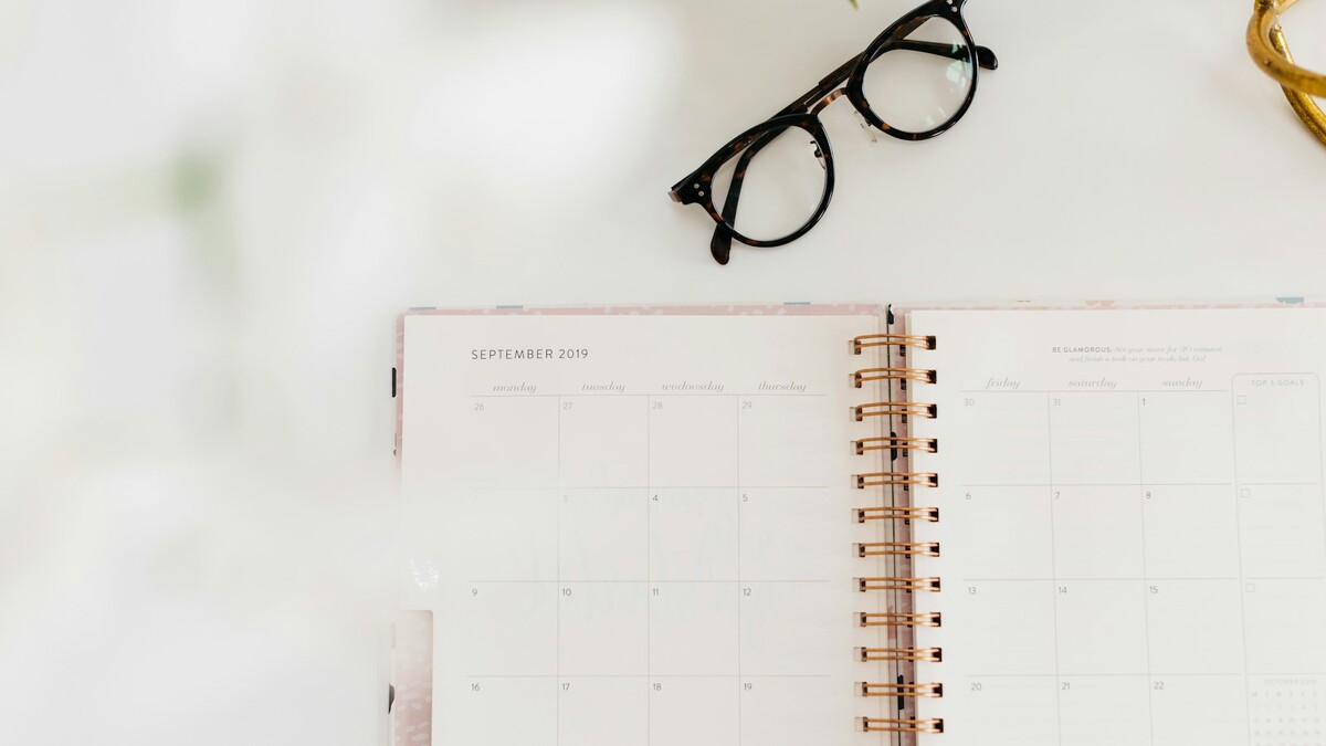 Qual a diferença entre jornada de trabalho e escala de trabalho? Agenda mensal aberta ao lado de óculos, usada para planejar dias de trabalho e folga