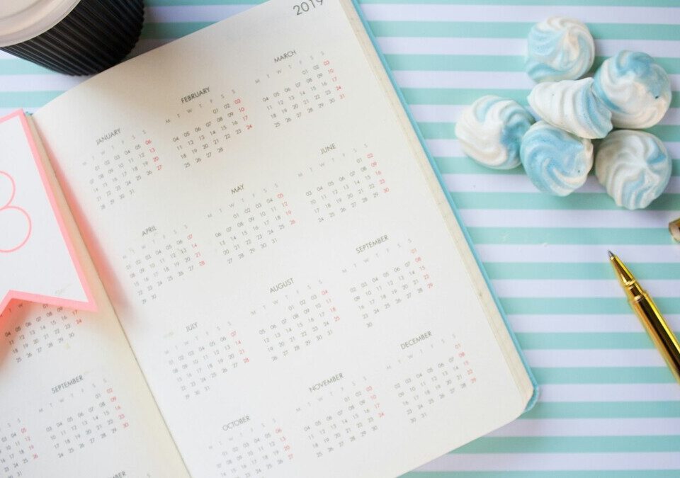 Agenda aberta com calendário do ano ao lado de uma caneta dourada
