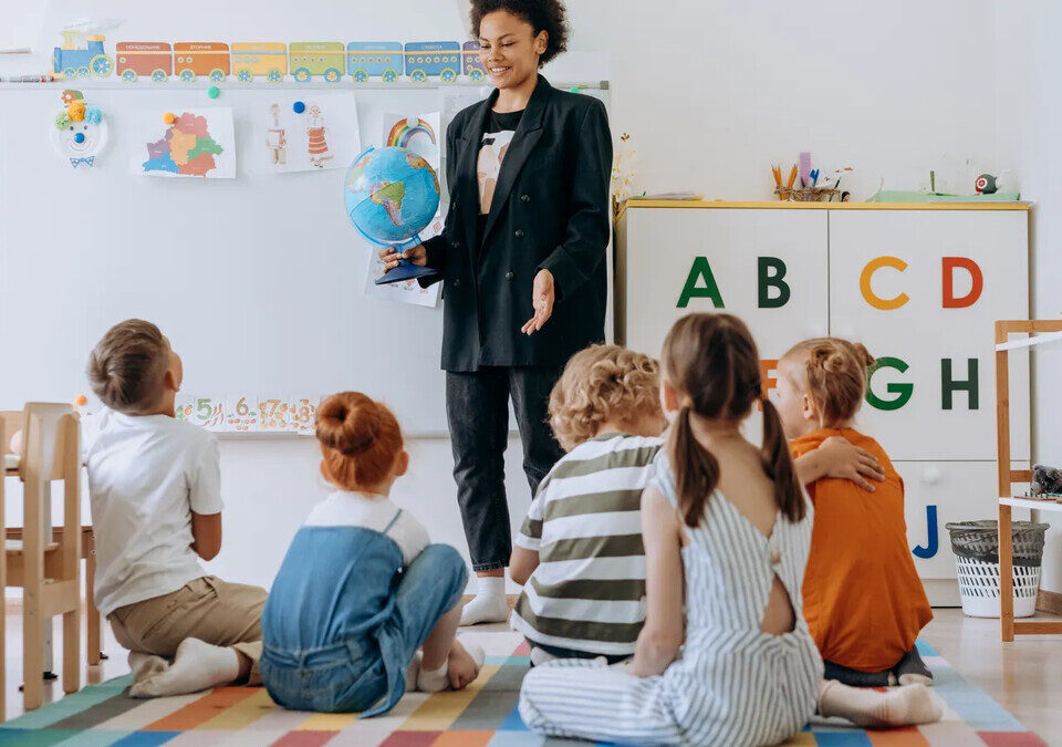 Professora realiza uma atividade educativa com crianças em sala de aula; imagem ilustrativa